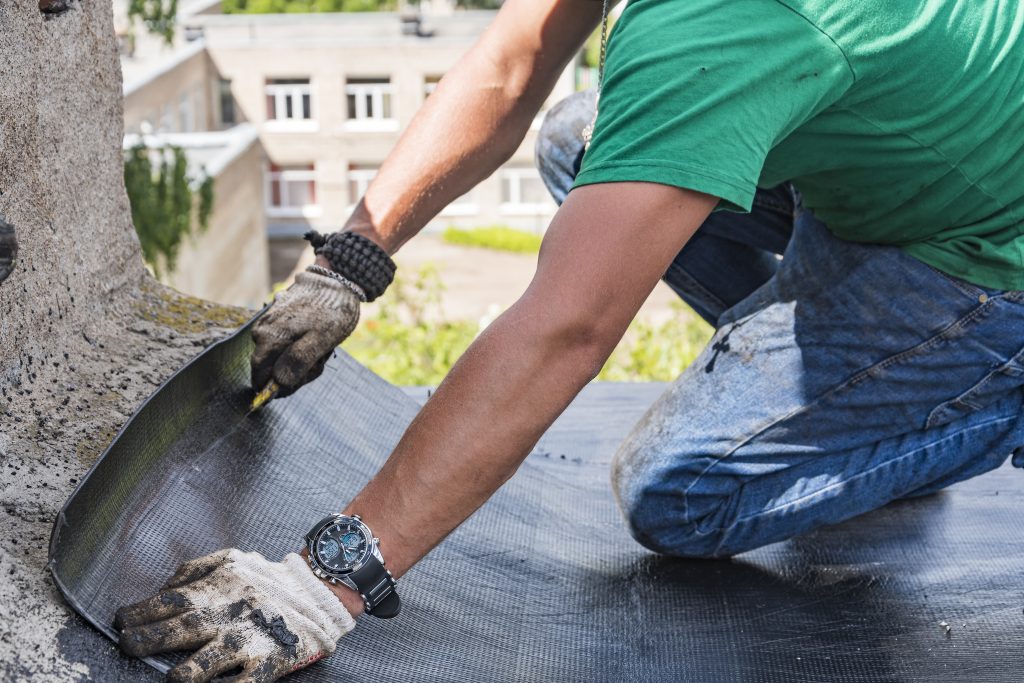 Worker performs overhaul of the roof of a residential building A construction worker cuts waterproofing material and prepares it for installation. Overhaul of the roof of the house.