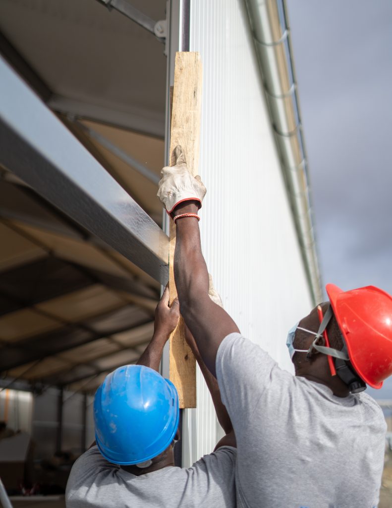 Afro-American builders wearing helmets and face masks while measuring the wall Two Afro-American builders wearing helmets and face masks while measuring the wall